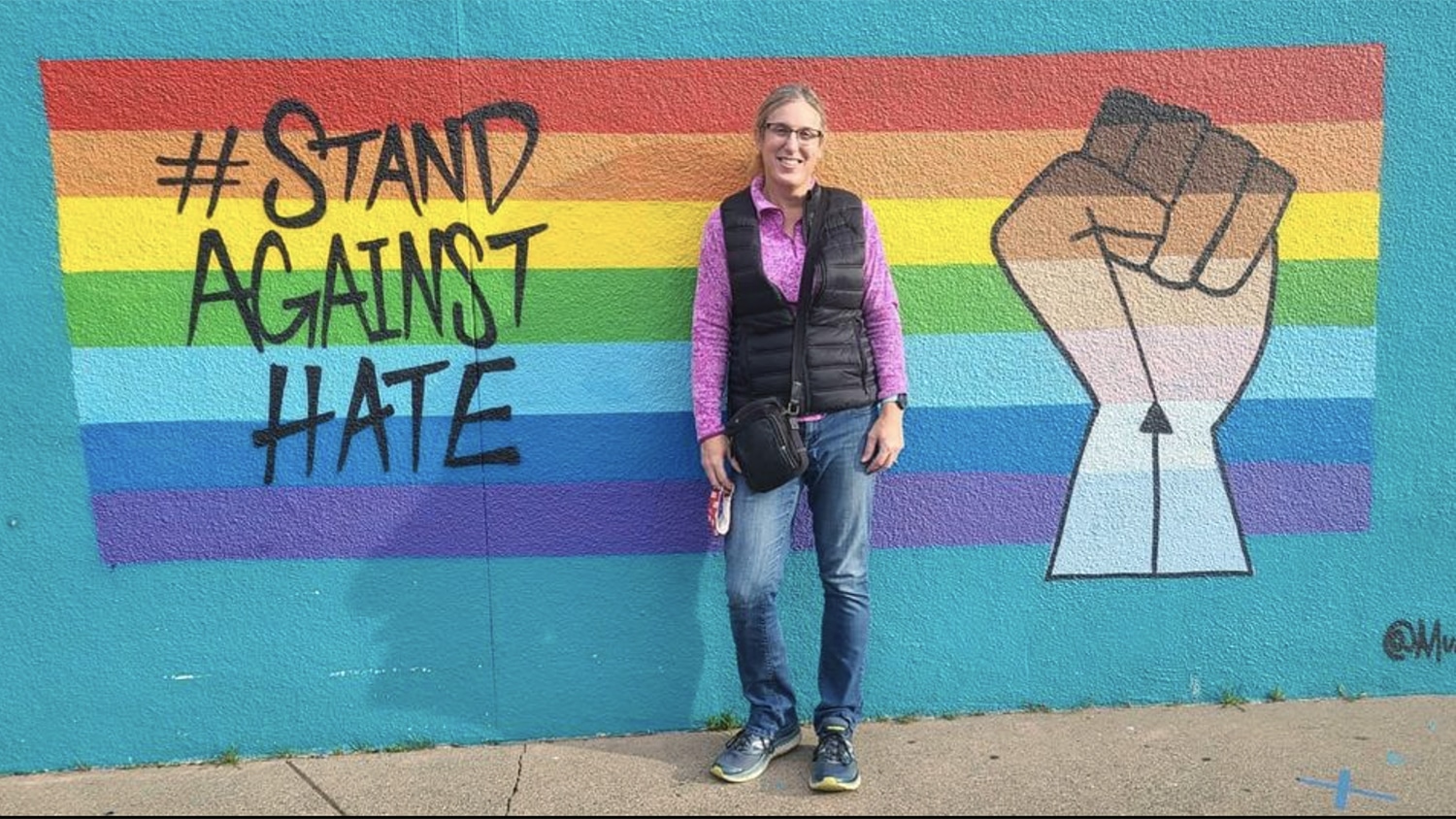 Alaina Brennan-Kupec in front of a rainbow flag.