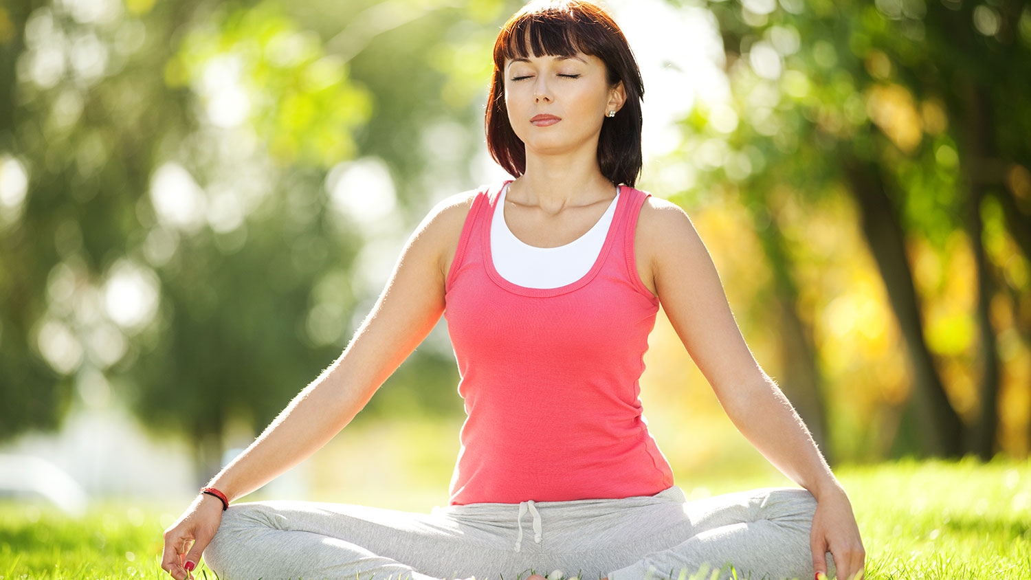 Woman in lotus yoga pose with eyes closed in a sunny meadow